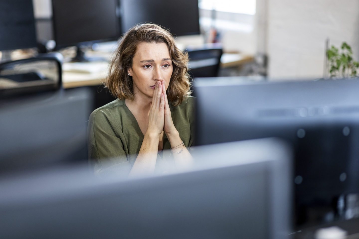 A stressed businesswoman sits in front of a desktop computer at an office.