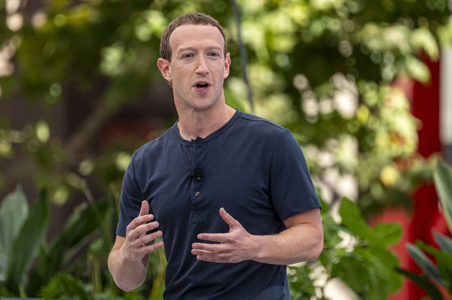 Mark Zuckerberg wears a dark t-shirt with a mic clipped on it and is outside, speaking.