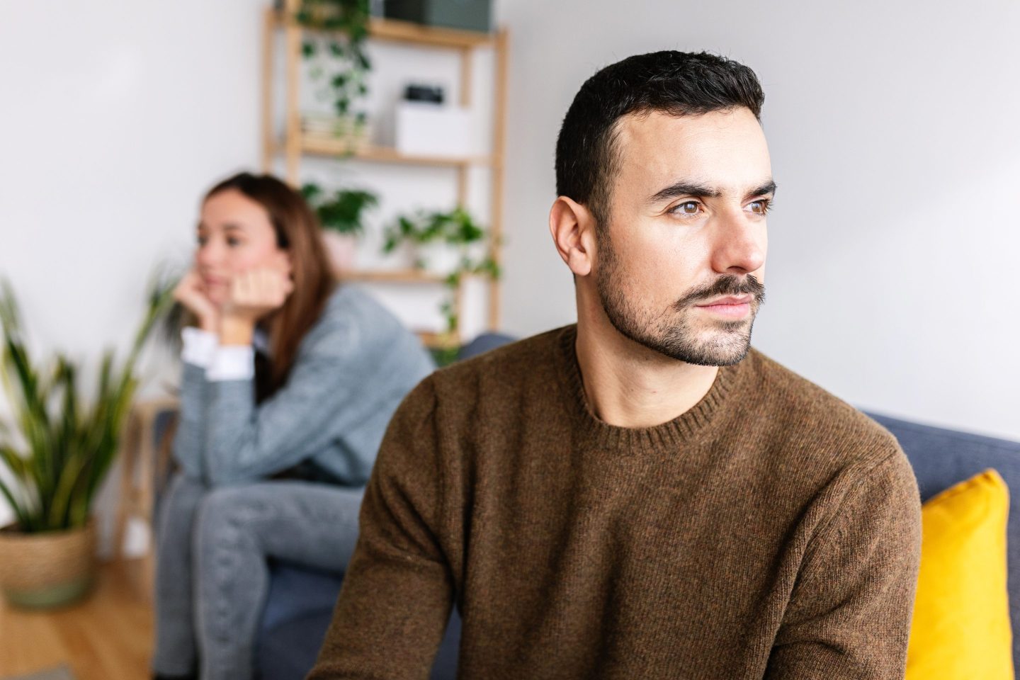 Young adult unhappy couple sitting distanced on sofa after arguing. Upset caucasian man looking annoyed away after having relationship problems with her girlfriend or wife.