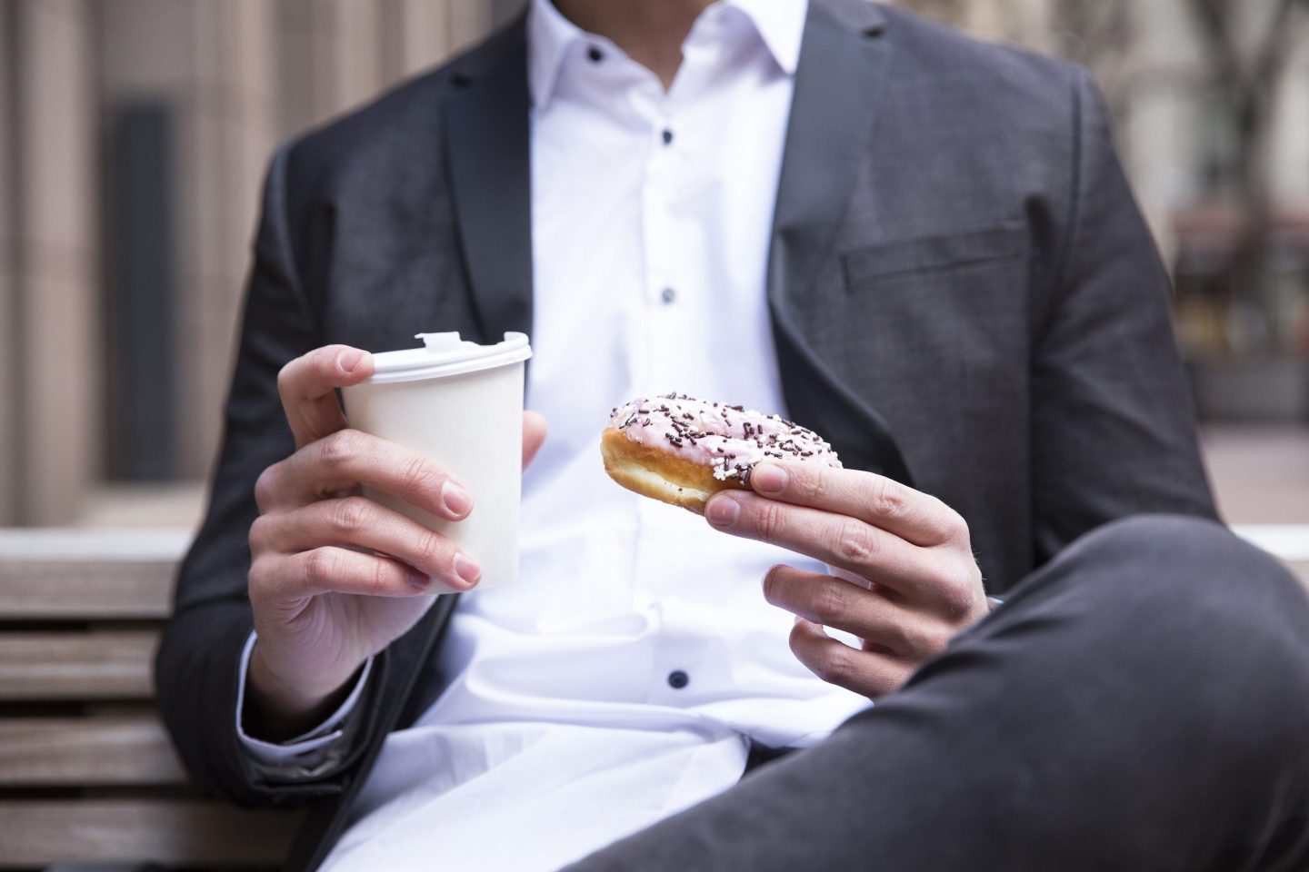 Businessman&#8217;s hands holding doughnut and coffee to go, close-up