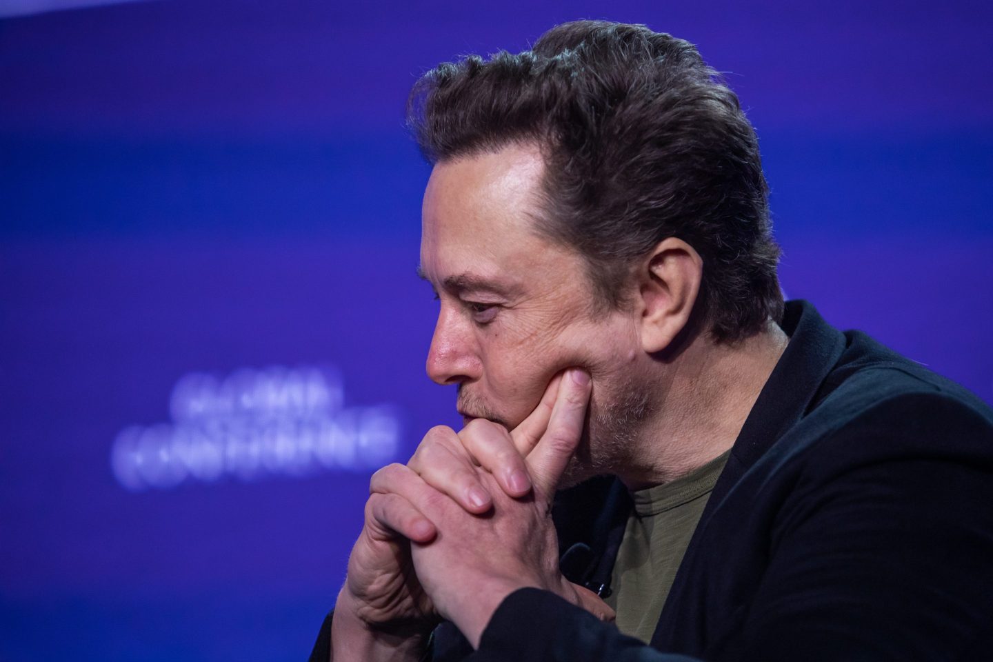 Elon Musk looks dejectedly to the side as he rests his head on his pointer fingers.