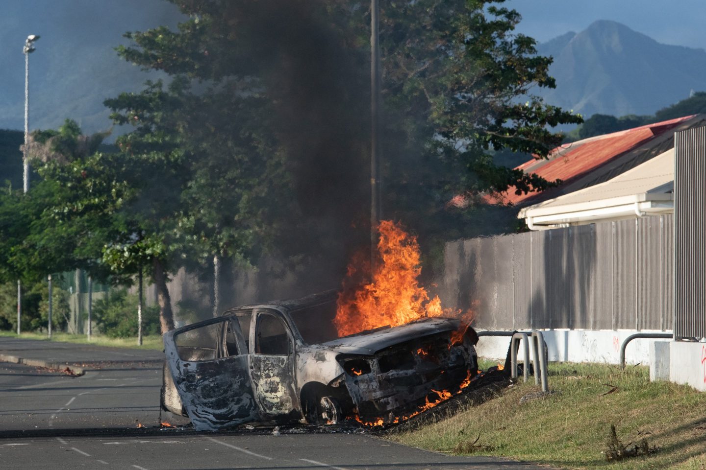 TOPSHOT &#8211; A car is burning on the Normandie provincial road, outside Noumea on May 16, 2024, amid protests linked to a debate on a constitutional bill aimed at enlarging the electorate for upcoming elections of the overseas French territory of New Caledonia. France deployed troops to New Caledonia&#8217;s ports and international airport, banned TikTok and imposed a state of emergency on May 16 after three nights of clashes that have left four dead and hundreds wounded. Pro-independence, largely indigenous protests against a French plan to impose new voting rules on its Pacific archipelago have spiralled into the deadliest violence since the 1980s, with a police officer among several killed by gunfire. (Photo by Delphine Mayeur / AFP) (Photo by DELPHINE MAYEUR/AFP via Getty Images)