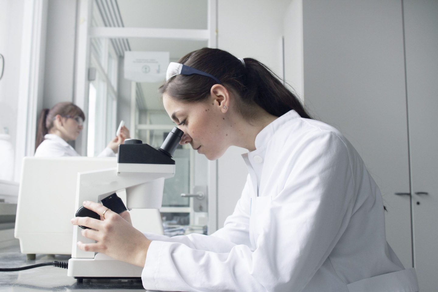 Stock image of a young woman wearing a lab coat and working in a labratory looking at something under a microsope.