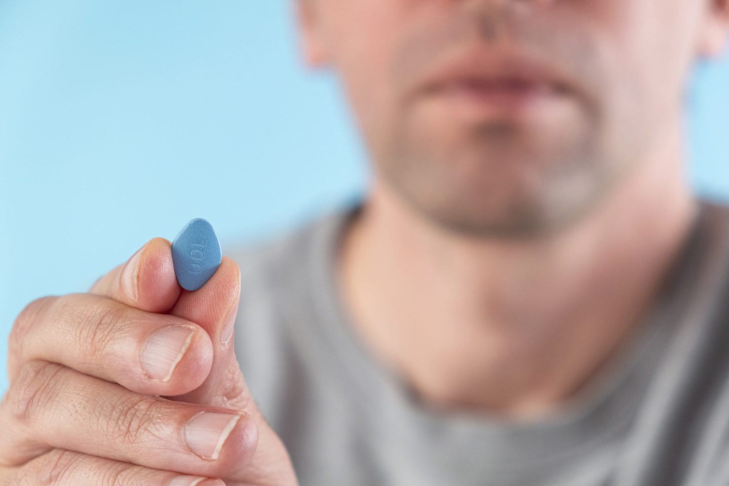 Man hold blue pill viagra in fingers on blue background. Medicine concept of men health, medication for potency, erection, treatment of erectile dysfunction Macro shot