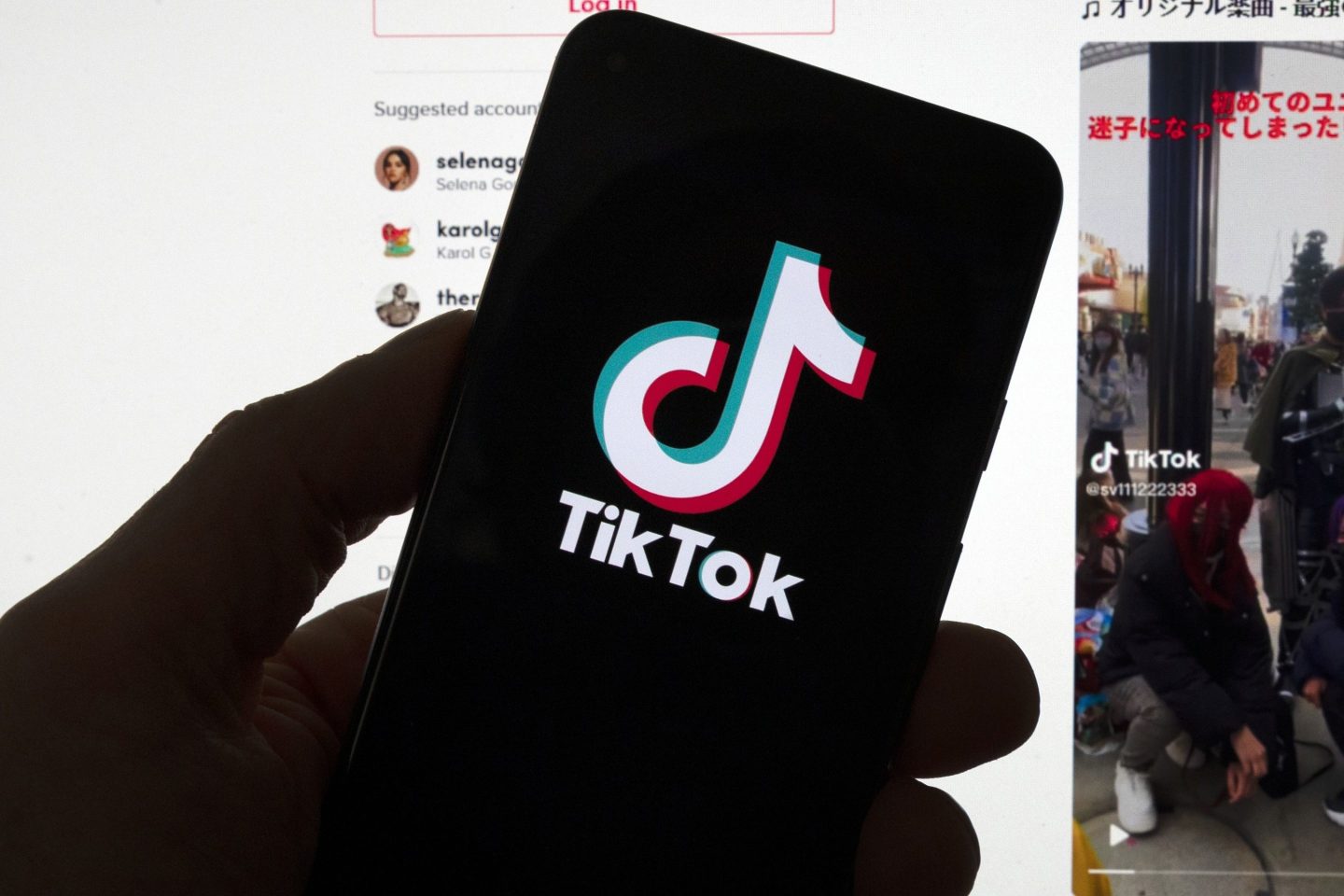 FILE &#8211; The TikTok logo is seen on a mobile phone in front of a computer screen which displays the TikTok home screen, March 18, 2023, in Boston. Social media platforms often rely on labels to let users know an account is operated by a Russian state propaganda agency. But new research shows that on TikTok at least, the labels aren&#8217;t very effective even when they&#8217;re applied consistently. (AP Photo/Michael Dwyer, File)