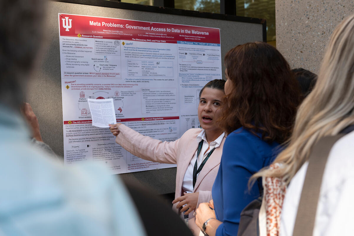 a woman in a pink jacket points to a red and white academic poster