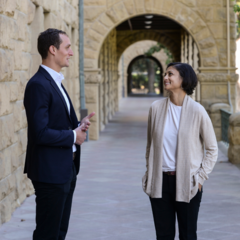 A man and a woman standing and talking at the entrance to Encina Hall, Stanford