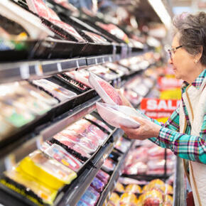 Woman shopping in grocery store, holding a package of meat