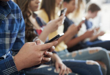 teens sitting side by side looking down at their phones