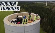 An aerial shot shows workers standing inside a wooden wind turbine as it is being constructed.