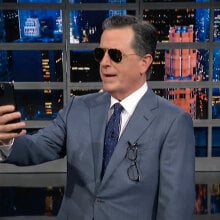 A man in a suit and sunglasses stares at a smartphone.