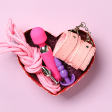 Box with toys from sex shop on color background
