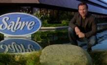 A man (Christian Slater on "The Office") kneeling next to a sign that reads "Sabre."