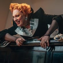 Jinkx Monsoon dressed as the Maestro atop a piano