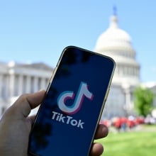 A phone displaying the TikTok logo in front of the White House. 