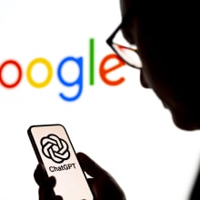 User looking at OpenAI ChatGPT logo on smartphone with Google logo in the background