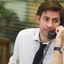 A man (John Krasinski as Jim Halpert on "The Office") sitting at a desk holding a phone to his ear.