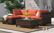 Wicker outdoor couch with red/orange cushion and table on patio with house siding, yard, and sandal in peripherals