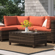Wicker outdoor couch with red/orange cushion and table on patio with house siding, yard, and sandal in peripherals