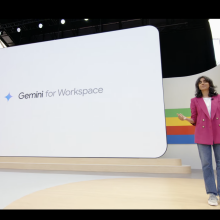 A woman on a stage in front of a screen with the words Gemini for Workspace