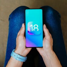 ios 18 logo on a smartphone being held in someone's hands on their lap