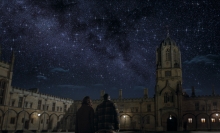 A couple looks up into the night sky on a university campus.