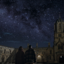 A couple looks up into the night sky on a university campus.