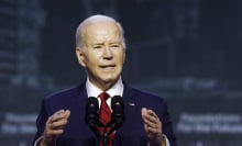 President Joe Biden standing behind a lectern in a navy suit and red tie. 