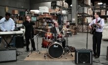 "The Office" cast members playing musical instruments in a warehouse.