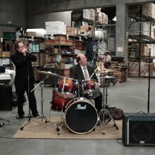"The Office" cast members playing musical instruments in a warehouse.