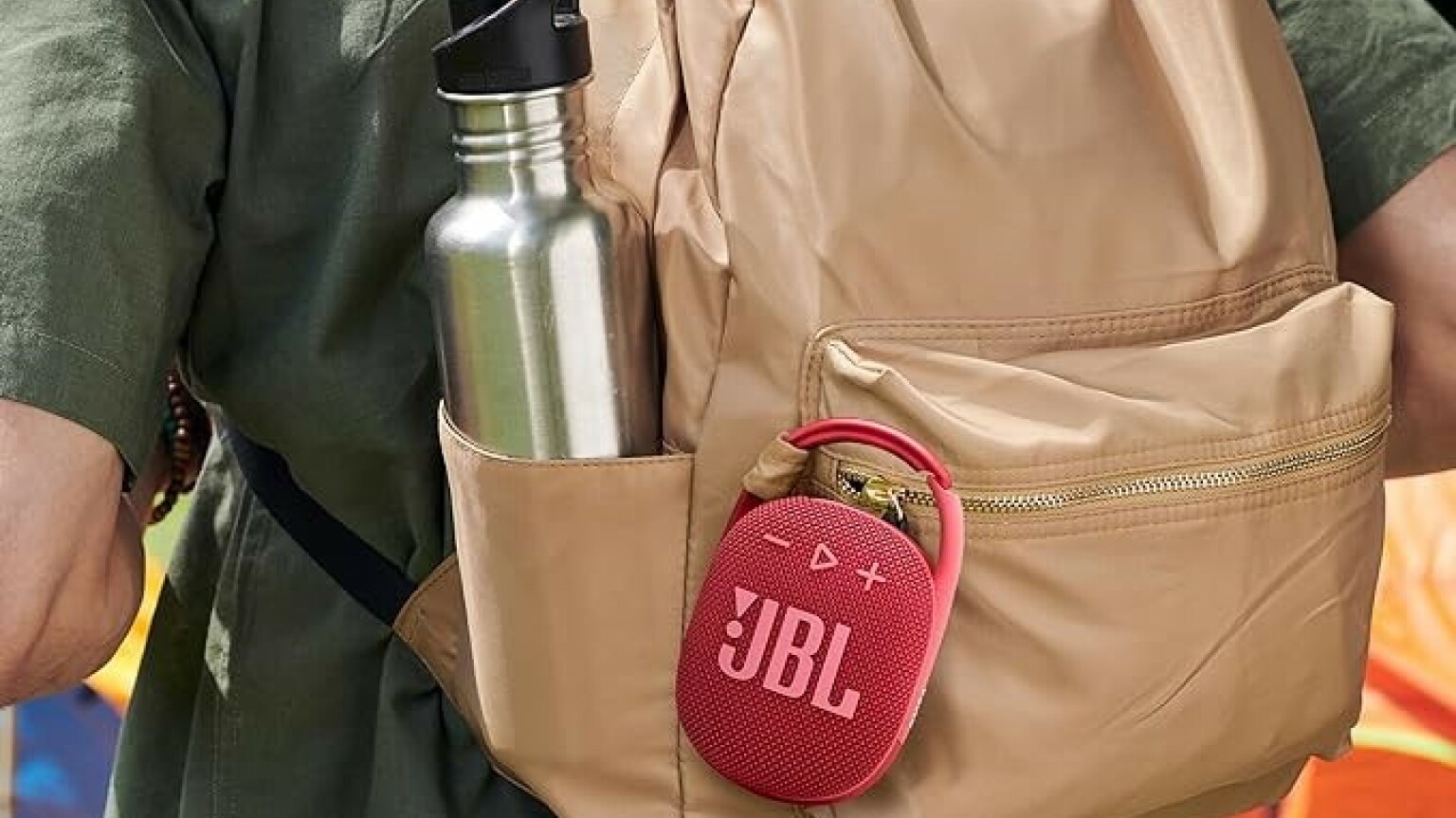 A JBL Clip 4 speaker is clipped onto a backpack