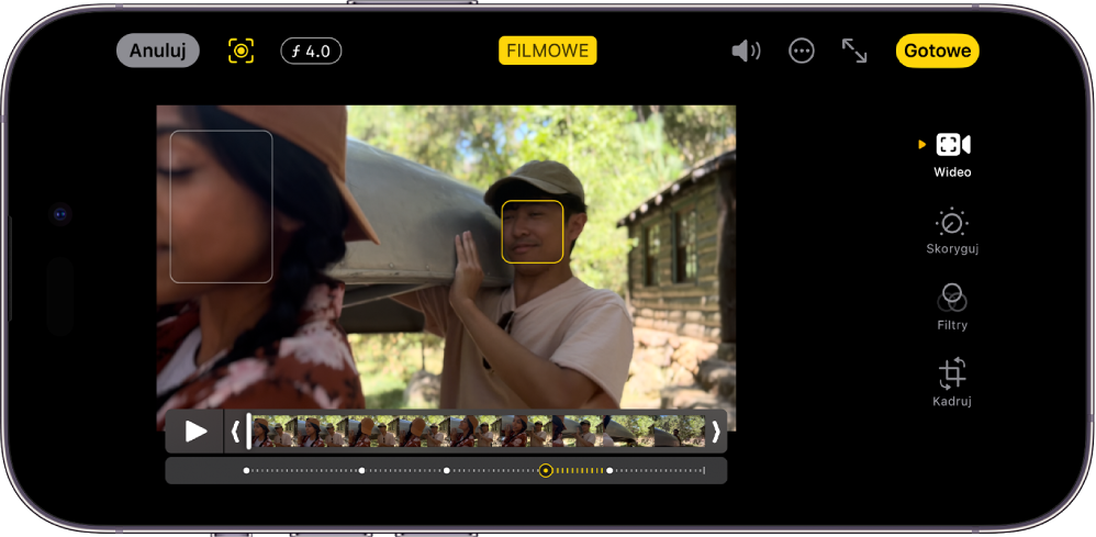 Ekran edycji wideo w trybie filmowym w orientacji poziomej. W lewym górnym rogu ekranu widoczny jest przycisk Anuluj, przycisk Fokus filmowy, ręcznie oraz przycisk Korekta głębi. U góry ekranu na środku znajduje się zaznaczony przycisk Filmowe. W prawym górnym rogu ekranu widoczny jest przycisk Głośność, przycisk Więcej opcji, przycisk Tryb pełnoekranowy oraz przycisk Gotowe. Na środku ekranu znajduje się wideo. Obiekt, na którym ustawiona jest ostrość, oznaczony jest ramką. Poniżej wideo widoczny jest podgląd klatek, wyświetlający miejsce w wideo, w którym następuje zmiana obiektu, na którym ustawiona jest ostrość. Po prawej stronie ekranu znajdują się przyciski edycji, od góry: Wideo, Skoryguj, Filtry oraz Kadruj.