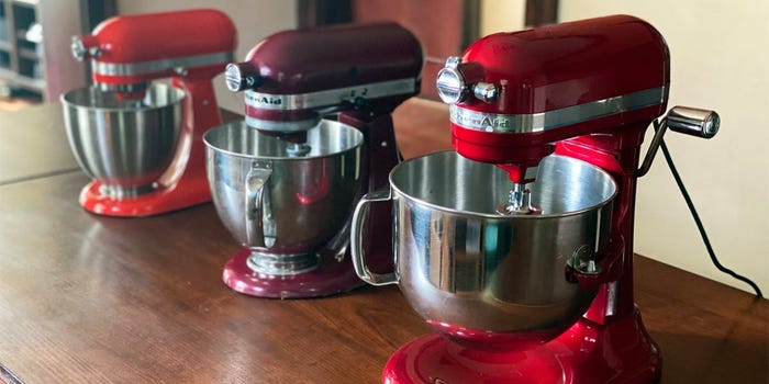 Three red Kitchenaid mixers on a table in a row.