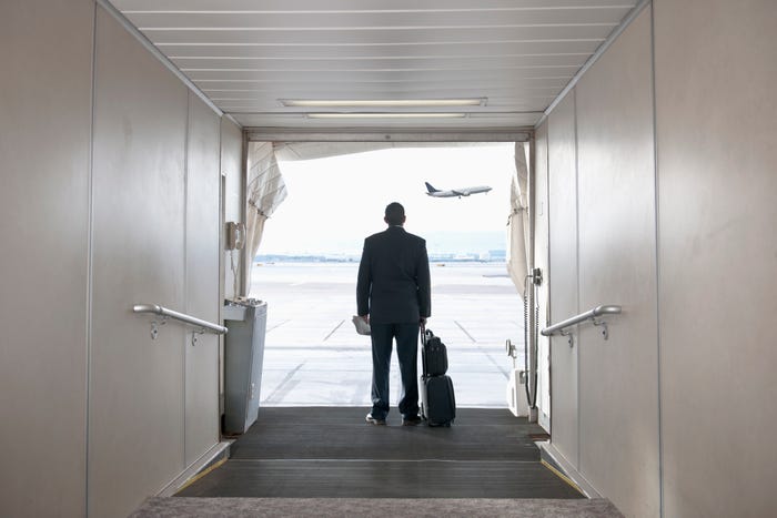 Man standing on jetway with luggage as plane leaves.