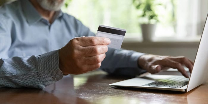A stock image shows an older man making a payment online using his credit card.