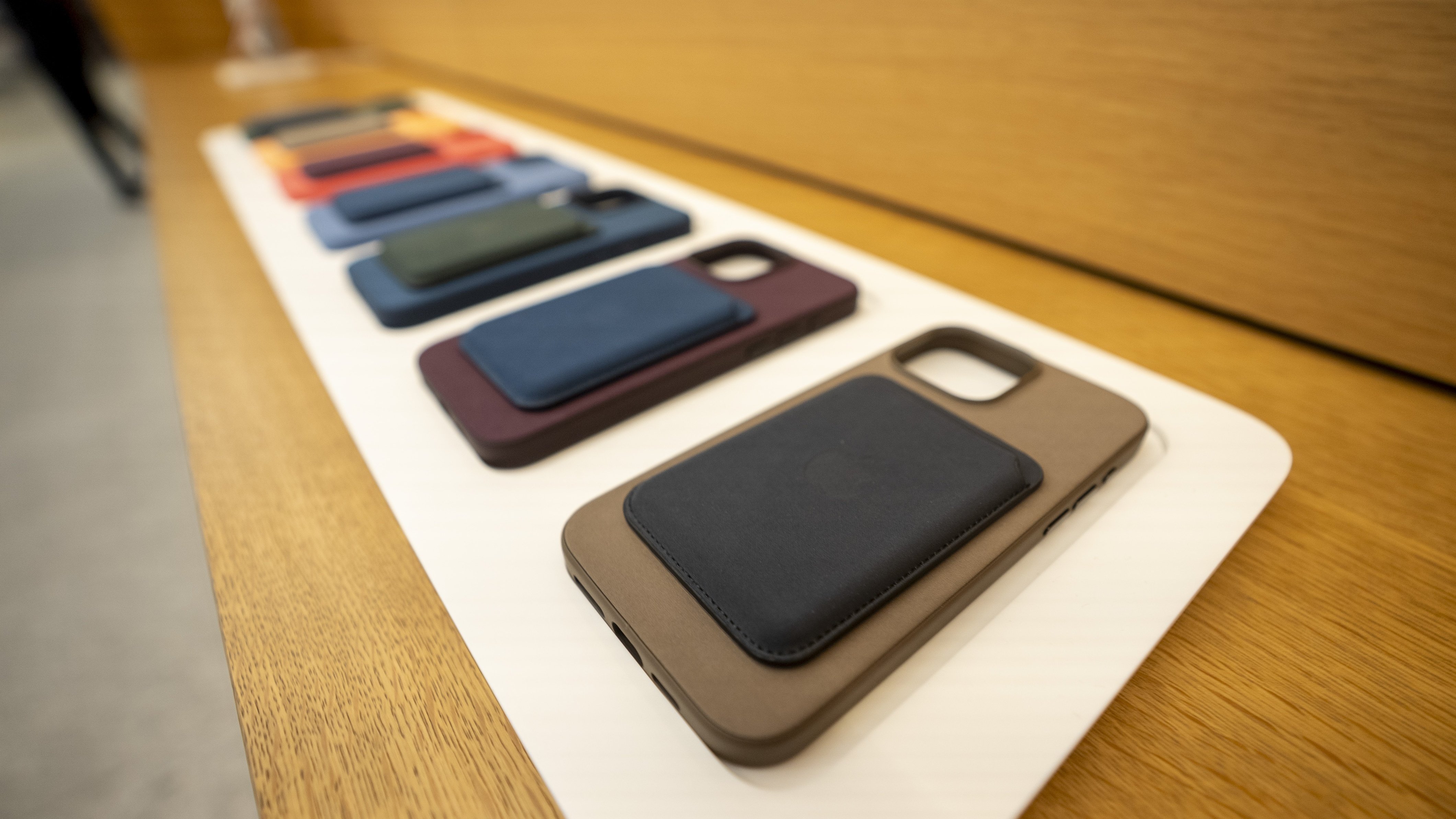 Photograph of more than five Apple iPhone FineWoven material cases lined up at a table in different colors, with optional wallet add-on attached.