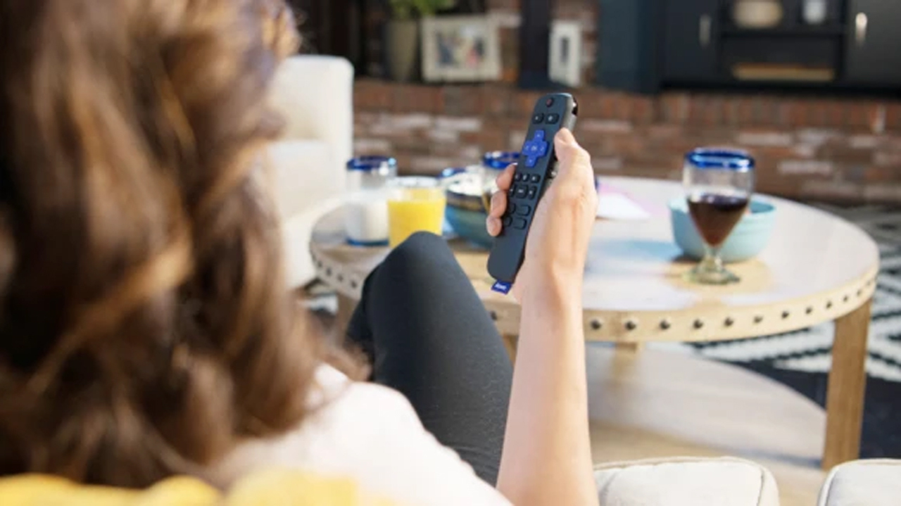 view from behind of woman sitting on sofa with Roku remote