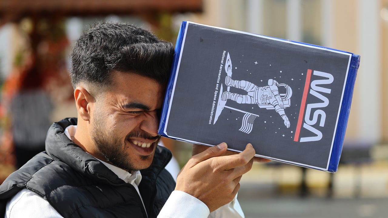 man looking at eclipse through a box with NASA on the side