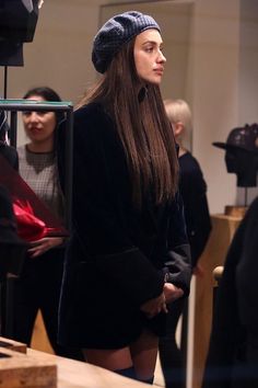 a woman with long hair wearing a black coat and hat standing in front of a group of people