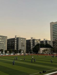 a group of people playing soccer on a field in front of some tall buildings with balconies