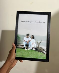 a person holding up a framed photo with an image of two people sitting on the grass