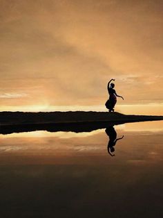 a woman is dancing in front of a body of water at sunset with her reflection