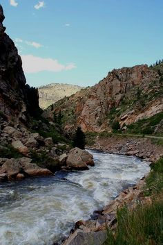 a river flowing between two rocky mountains under a blue sky