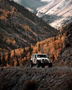 a jeep is parked on the side of a mountain with fall colored trees in the background