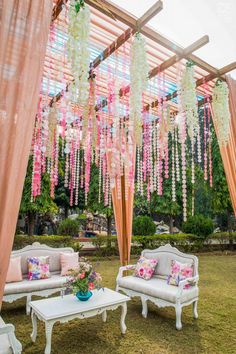 an outdoor seating area with pink and white flowers hanging from the ceiling