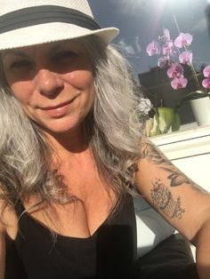 a woman with grey hair wearing a white hat and black dress sitting in front of flowers