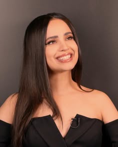 a woman with long hair smiling and wearing a black dress on top of a gray wall