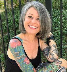 a woman with grey hair and tattoos on her arm sitting in front of a fence