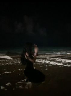 a woman kneeling down on the beach at night