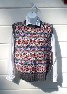 a sweater vest hanging on a white wall next to a hanger with a red and blue pattern